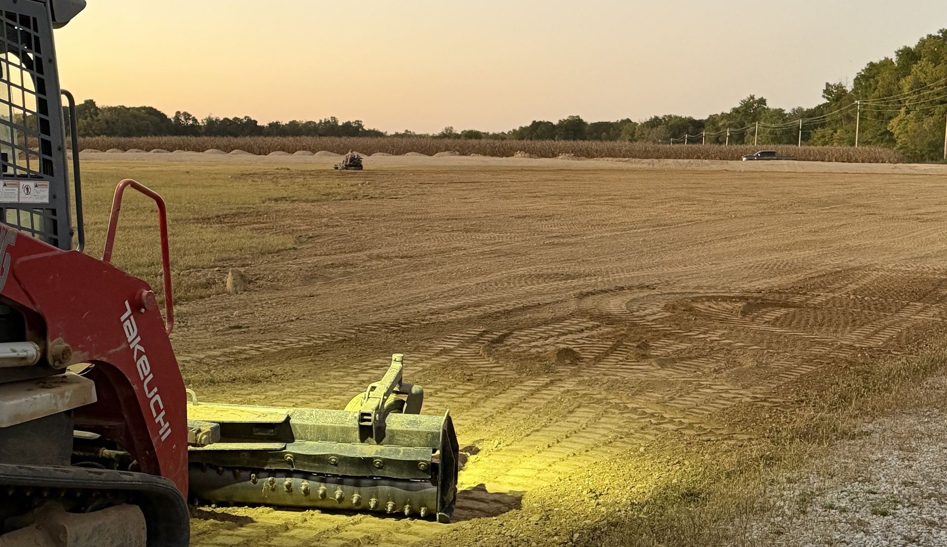 A track loader with a soil conditioner on a freshly graded field at sunset